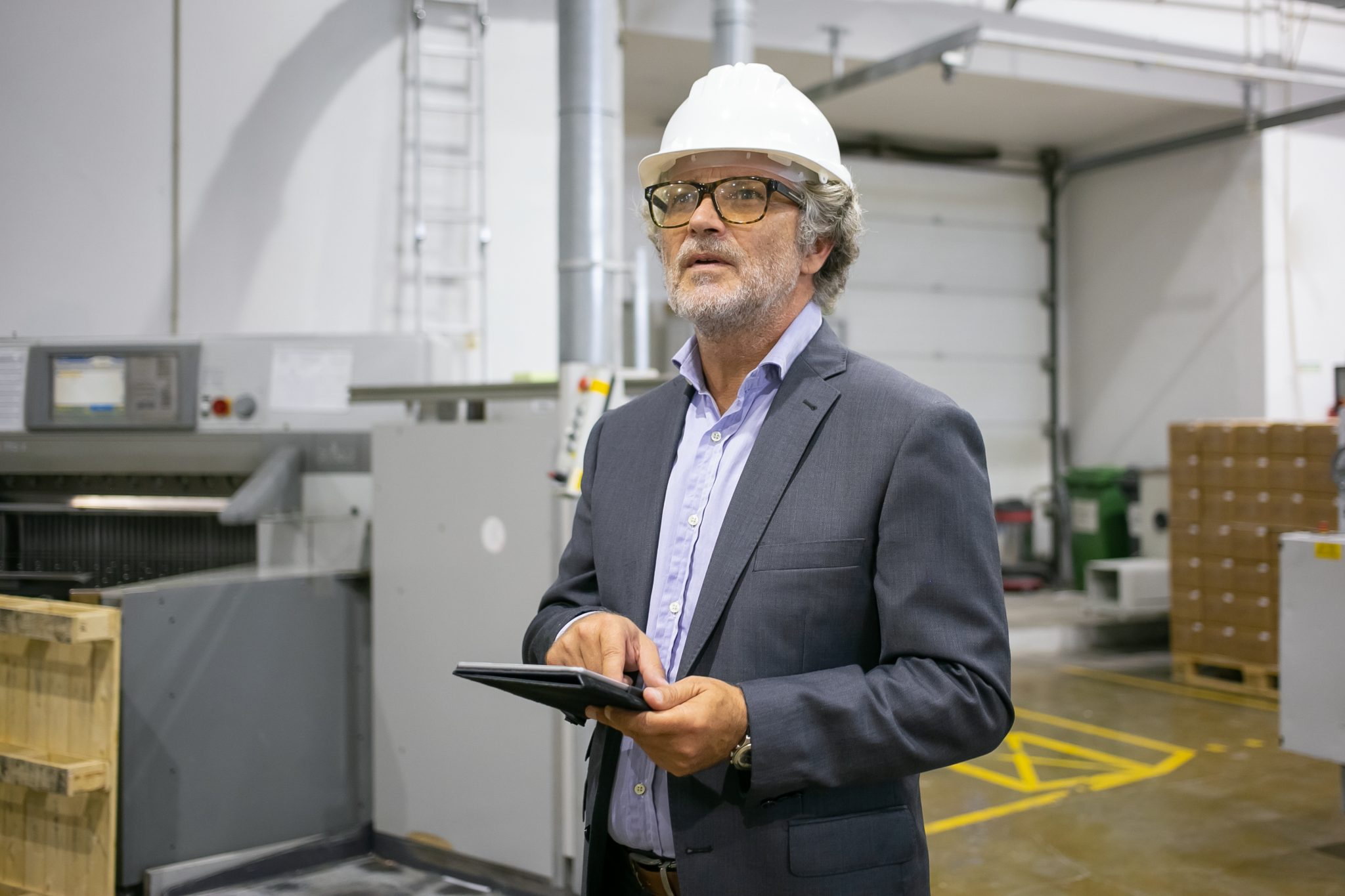pensive man in protective helmet holding tablet and looking away